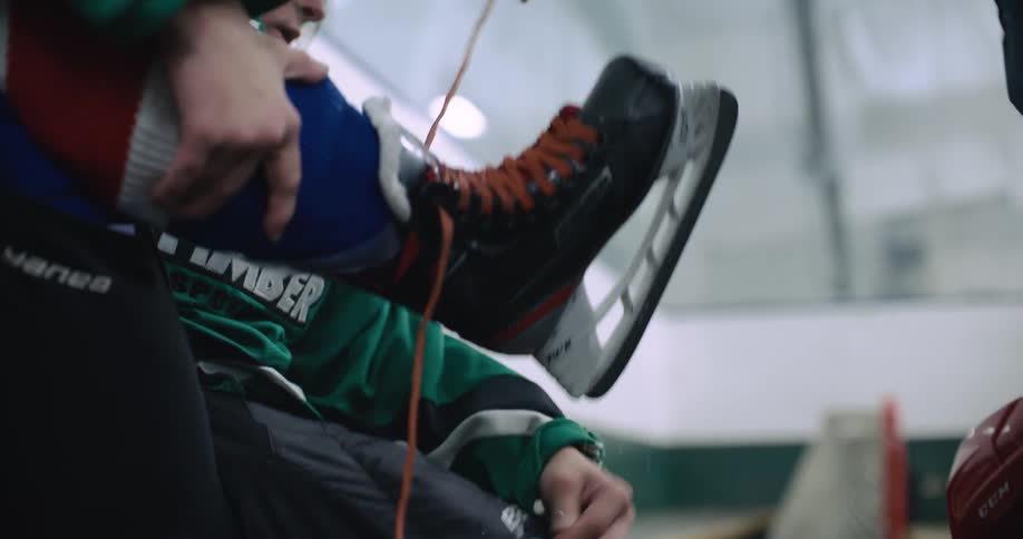 Girl sitting on a bench in the ice hockey rink gets her mother to help her to take off the skates