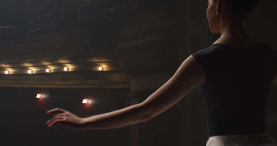A ballerina dances on a stage in a dimly lit theater