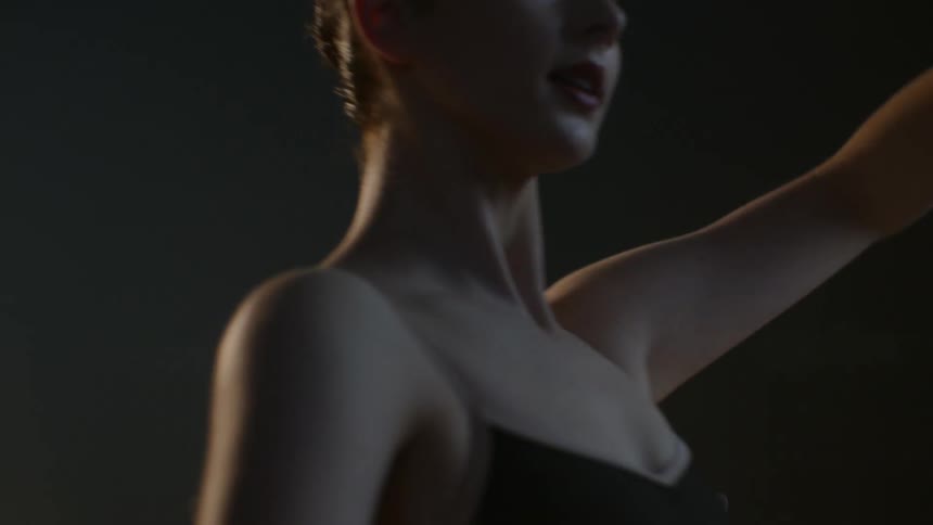 Ballerina moves through dance poses as she practices with standing bar under theater lights