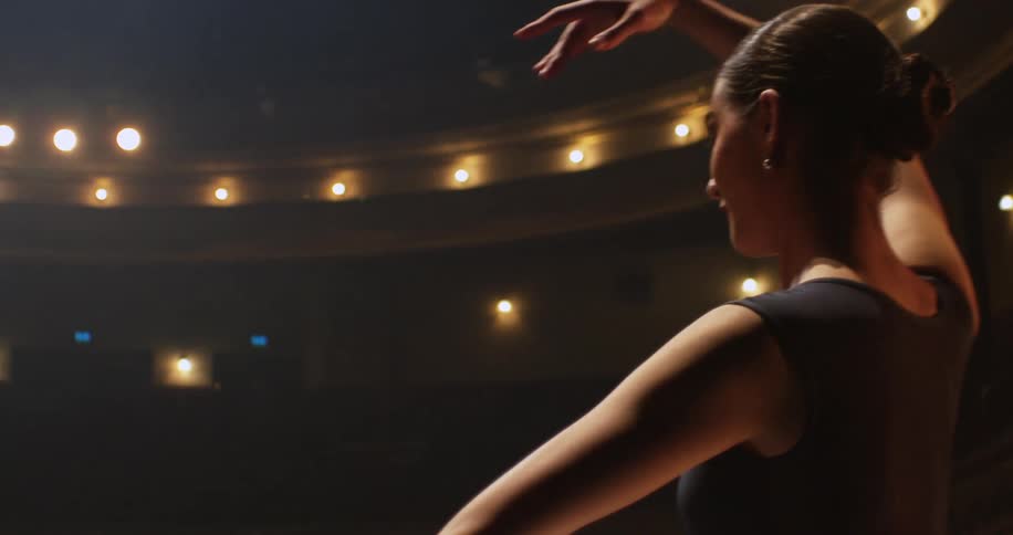 Woman moves through dance pose in empty theater