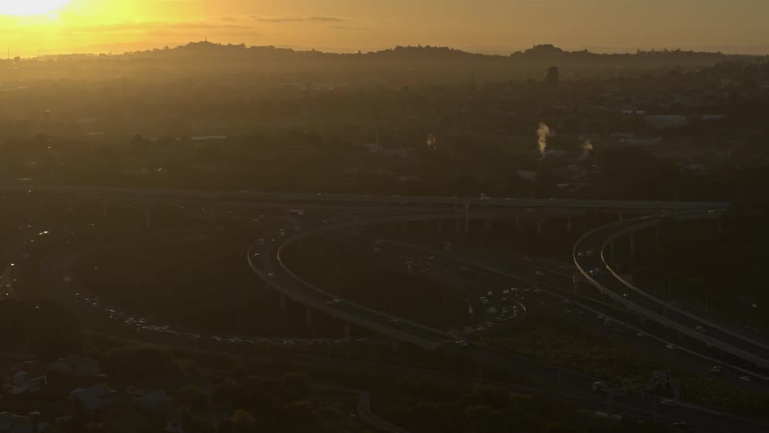Fog obscures city under a crimson sky as traffic flows along multiple highways and overpasses