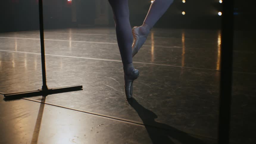 Ballerina practice en pointe using freestanding bar on stage in theater