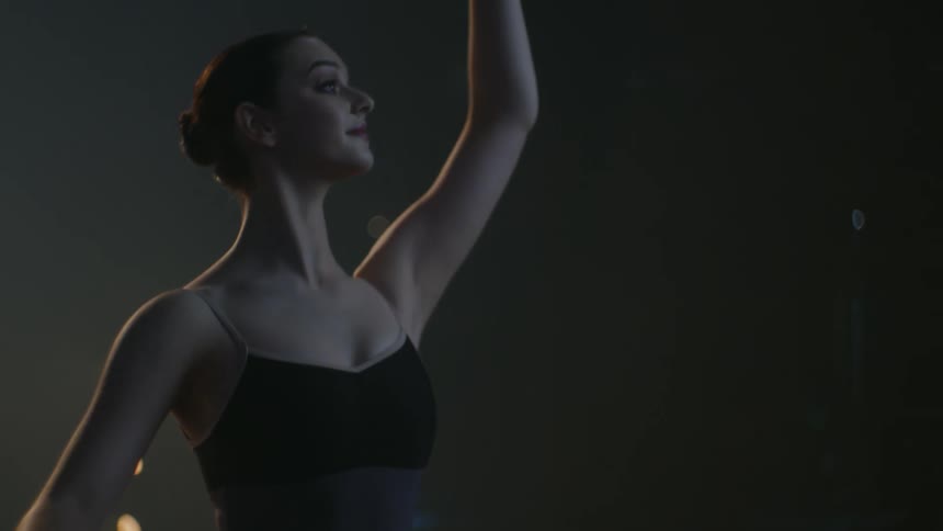 A woman holds on to a barre and practices ballet moves