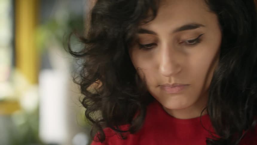 Woman with dark wavy hair and red sweater looks down in the kitchen
