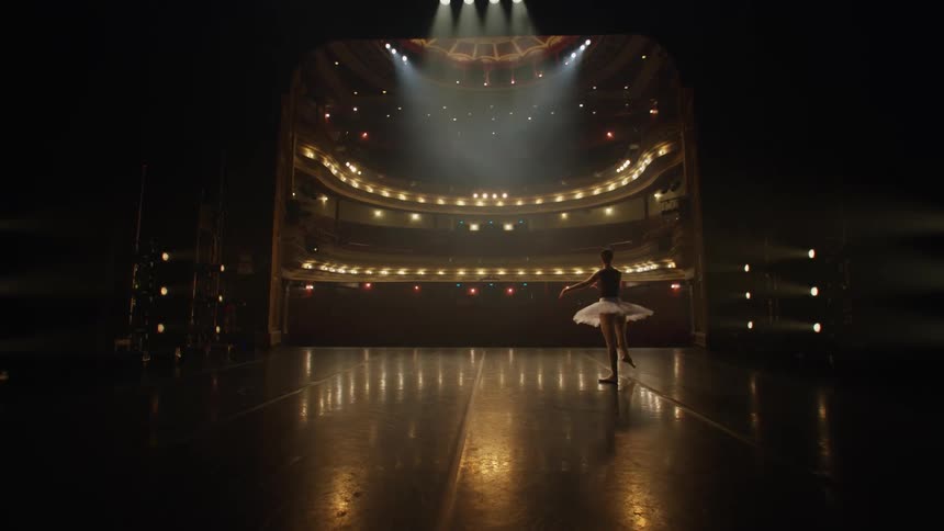 Young ballerina practices ballet movements on an empty theatre stage