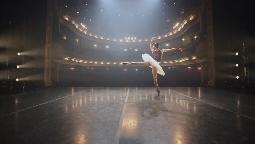 A ballerina dances on stage under bright spotlights in an empty theater