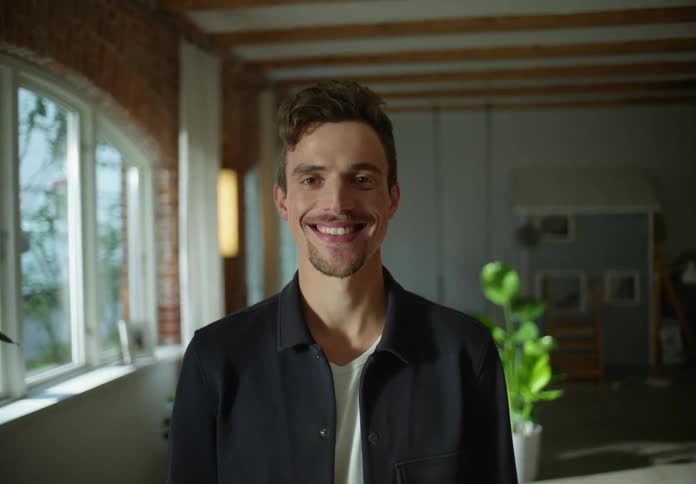 Young man standing on a room at home looks at the camera and smiles