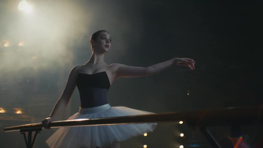 Young ballerina practices ballet poses on a stage under a spotlight