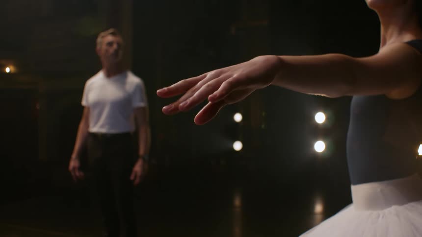 A man stands on a stage and watches as a ballerina moves her arms around
