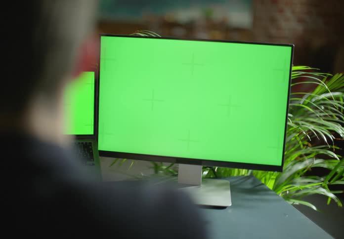 A man is sitting at a desk facing computer screens
