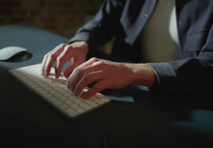 A man is typing on a keyboard with a computer mouse next to him on the table