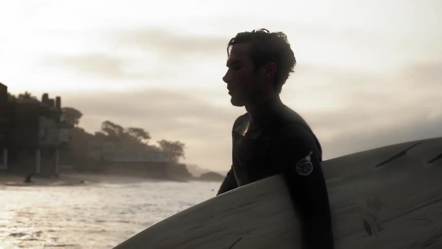 A man carries a surfboard out of the water and up the beach
