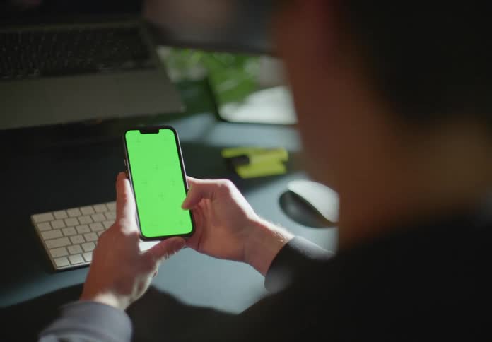 Young man sitting at a desk uses a smartphone with a green replaceable screen