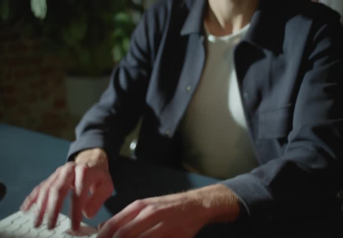 Young man sitting at a desk typing on a white keyboard at home