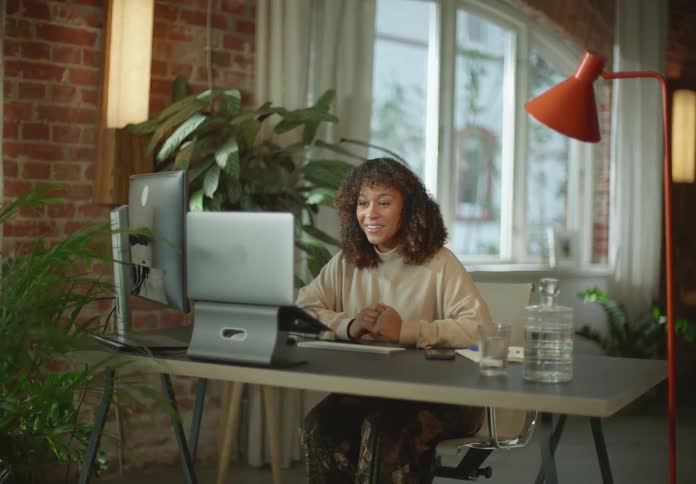 Young happy woman talking on a video call in front of a computer over a desk at home