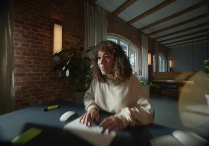 A woman sitting at a desk at home types on her computer and then looks really happy with what she sees