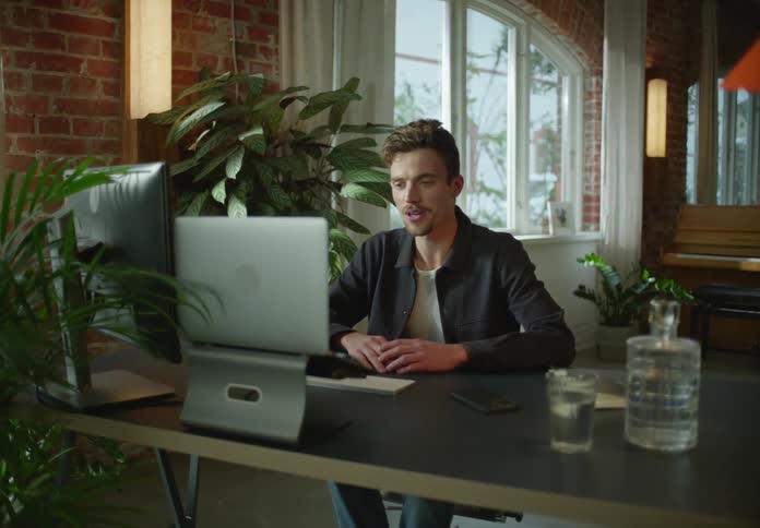Young man talking on a video call through a laptop over a desk at home