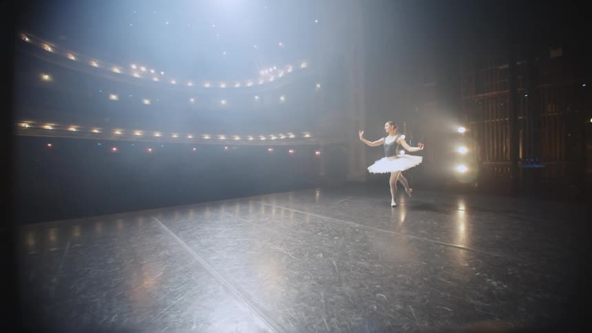 A ballerina dances across an empty stage in a theater