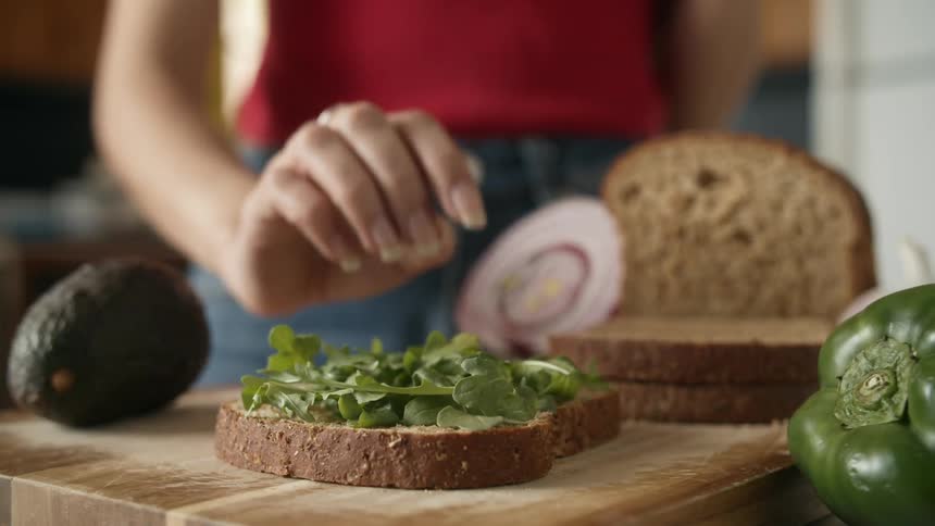 Womans hand patting down lettuce on a slice of wheat bread