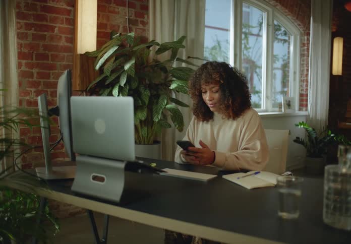 A woman checks her smartphone while sitting at her desk