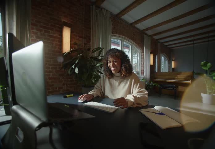 A woman laughs to herself while working on her computer in an office