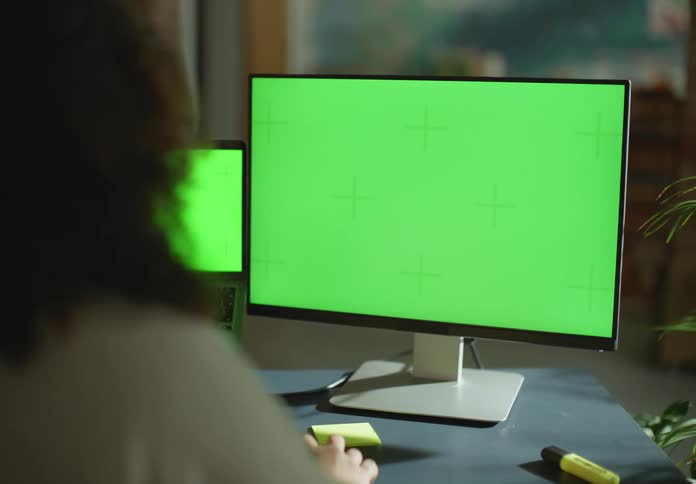 Woman works at table with laptop and a larger monitor