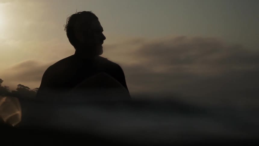 A man sits on a surfboard near sunset