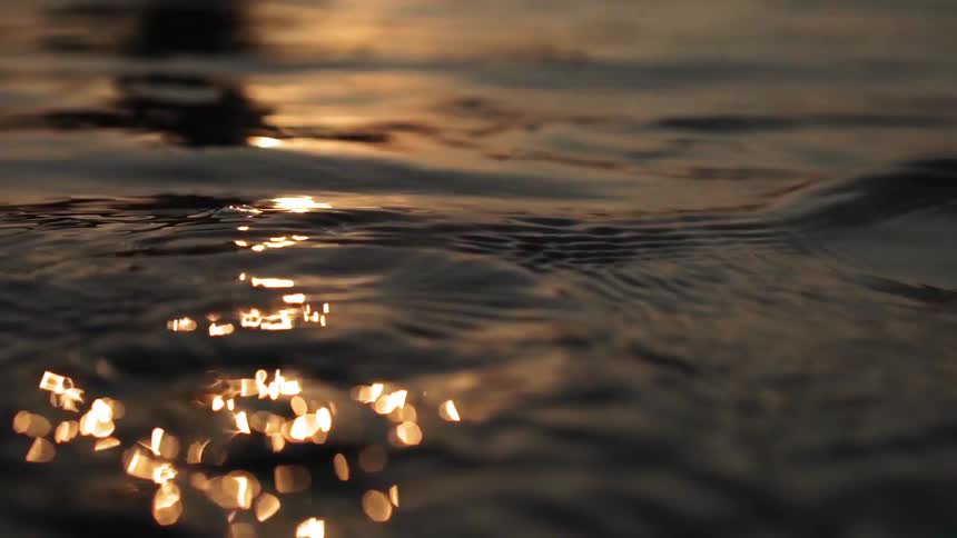 A man is sitting on a surfboard in the water at dawn