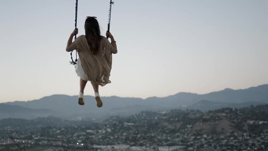 A woman is swinging on a hillside over a town