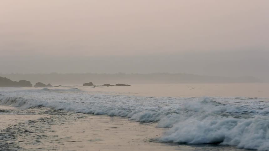 Waves crash on the shore on a foggy day