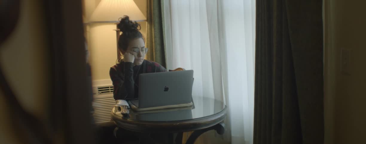 A young woman uses a laptop while sitting at a small table indoors during the day