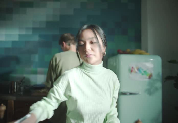 A woman hands a friend a bowl of salad to set on their kitchen table