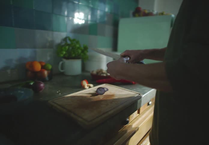 A man smiles as he looks down cutting up vegetables in his kitchen