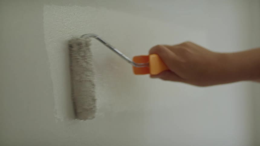 A man repaints a while wall with white paint
