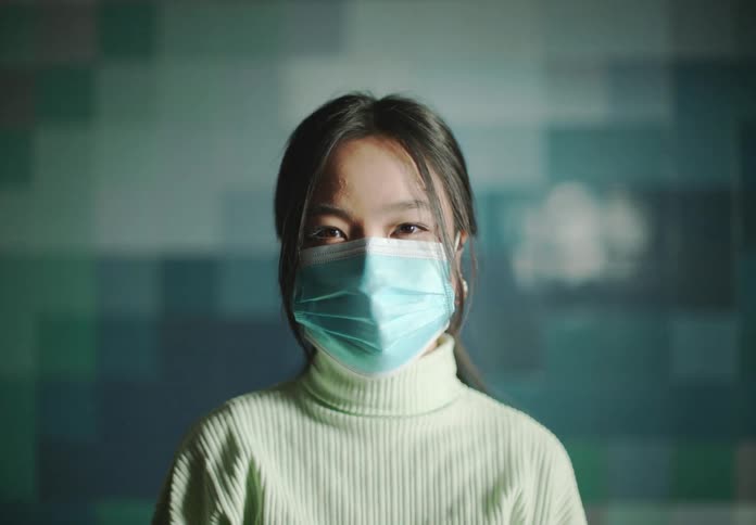 A woman wears a face mask while standing in front of a colorful pixelated wall
