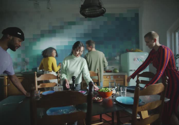 A group of young women and men set a dinner table in a kitchen