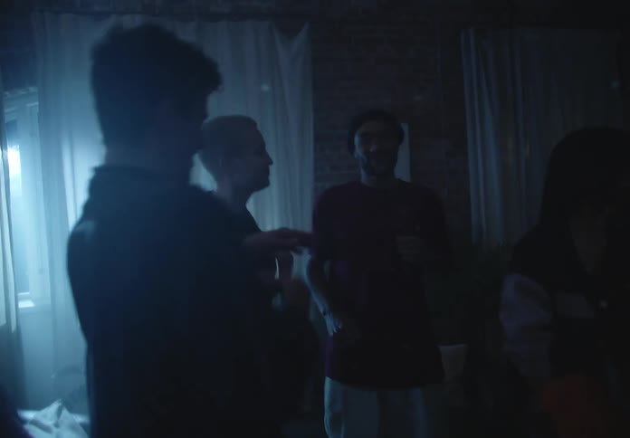 A group of friends dance under strobing lights in their apartment