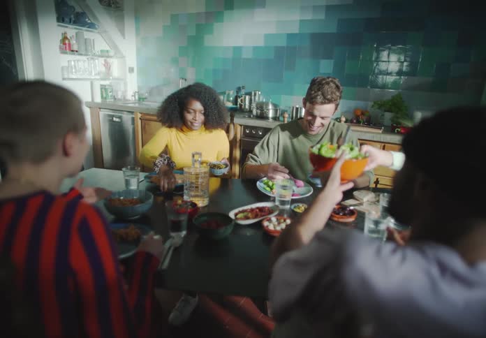 Friends smile as they sit at dinner table in kitchen passing food