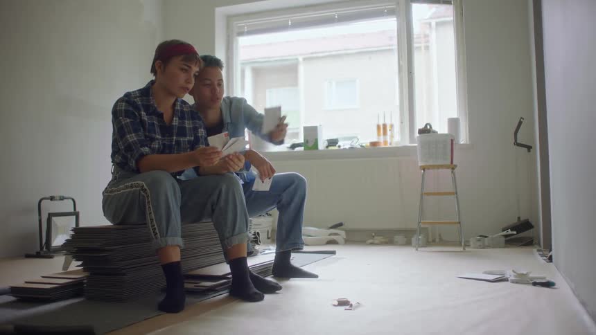 Two people sit on stack in room being remodeled contemplating paint colors