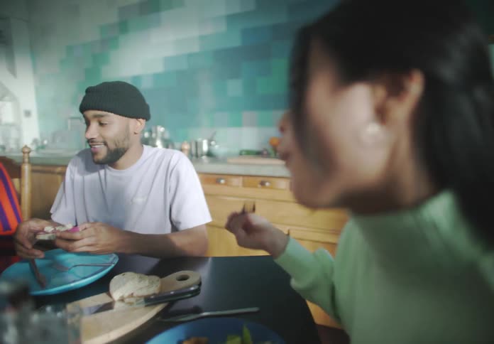 A group of people sit around a kitchen table eating food and talking