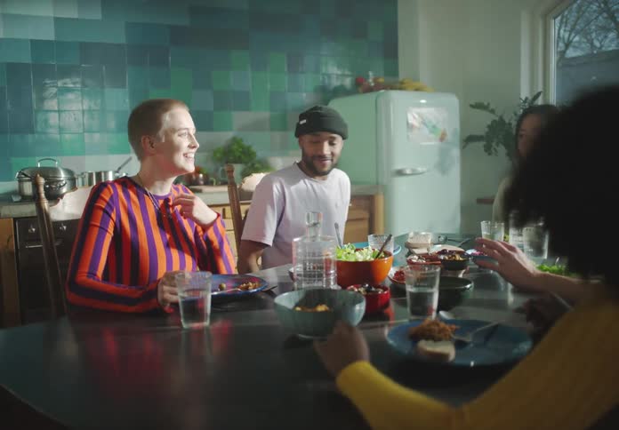A group of young men and women sit around a dining table together talking and laughing