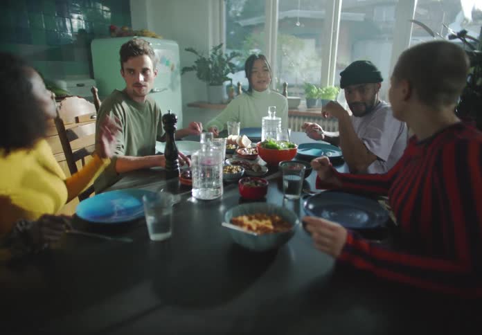 A group of young adults sit around a dining table talking