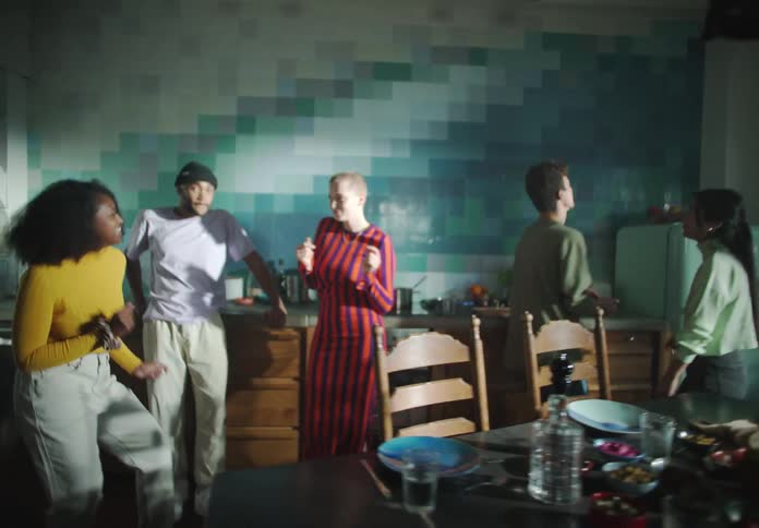 Friends dance around in area between stove and table strewn with food