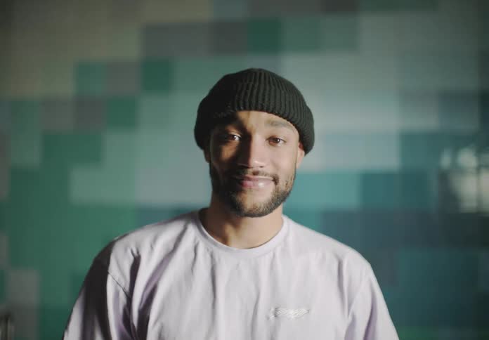 A man touches his beanie as he stands indoors