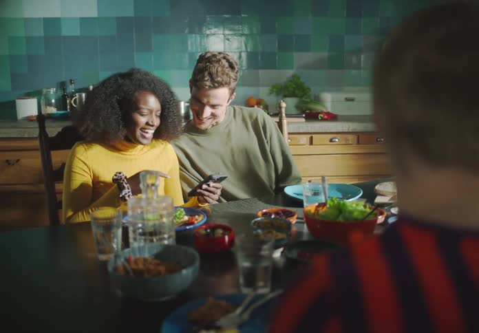 A group of people are sitting at a kitchen table full of food talking and laughing