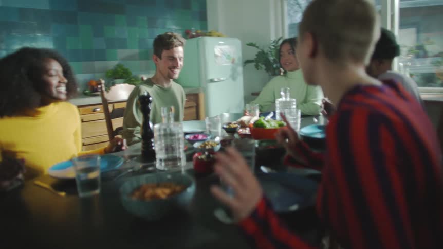 A group of young men and women sit around a dining table of food