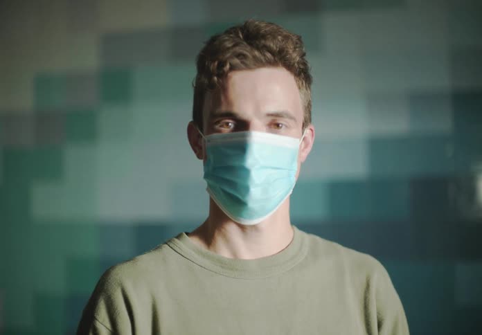 Man with blue mask and green sweater faces the camera with eye contact