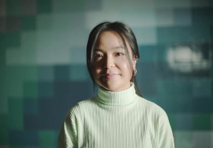 Woman with straight hair earrings and white turtleneck sweater faces the camera with eye contact