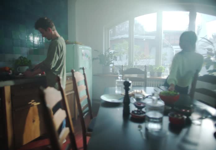 A group of people cook and set a dining table together in a house during the day