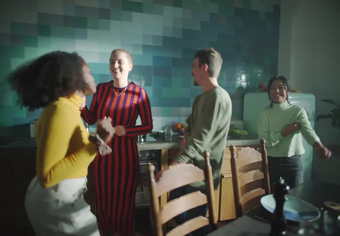 A group of friends dances around dining table in the kitchen